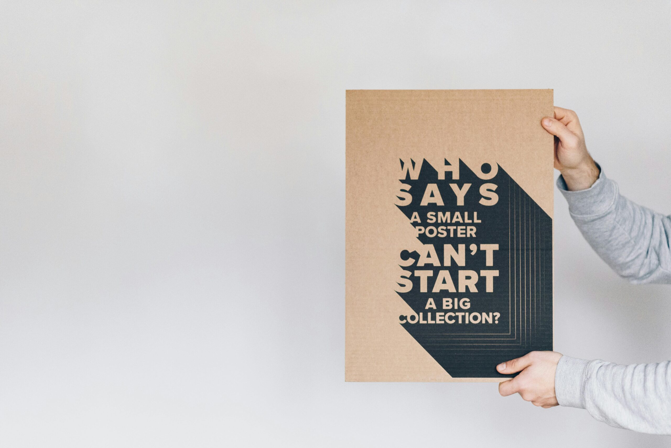 Hands holding a motivational poster with bold typography against a white background.